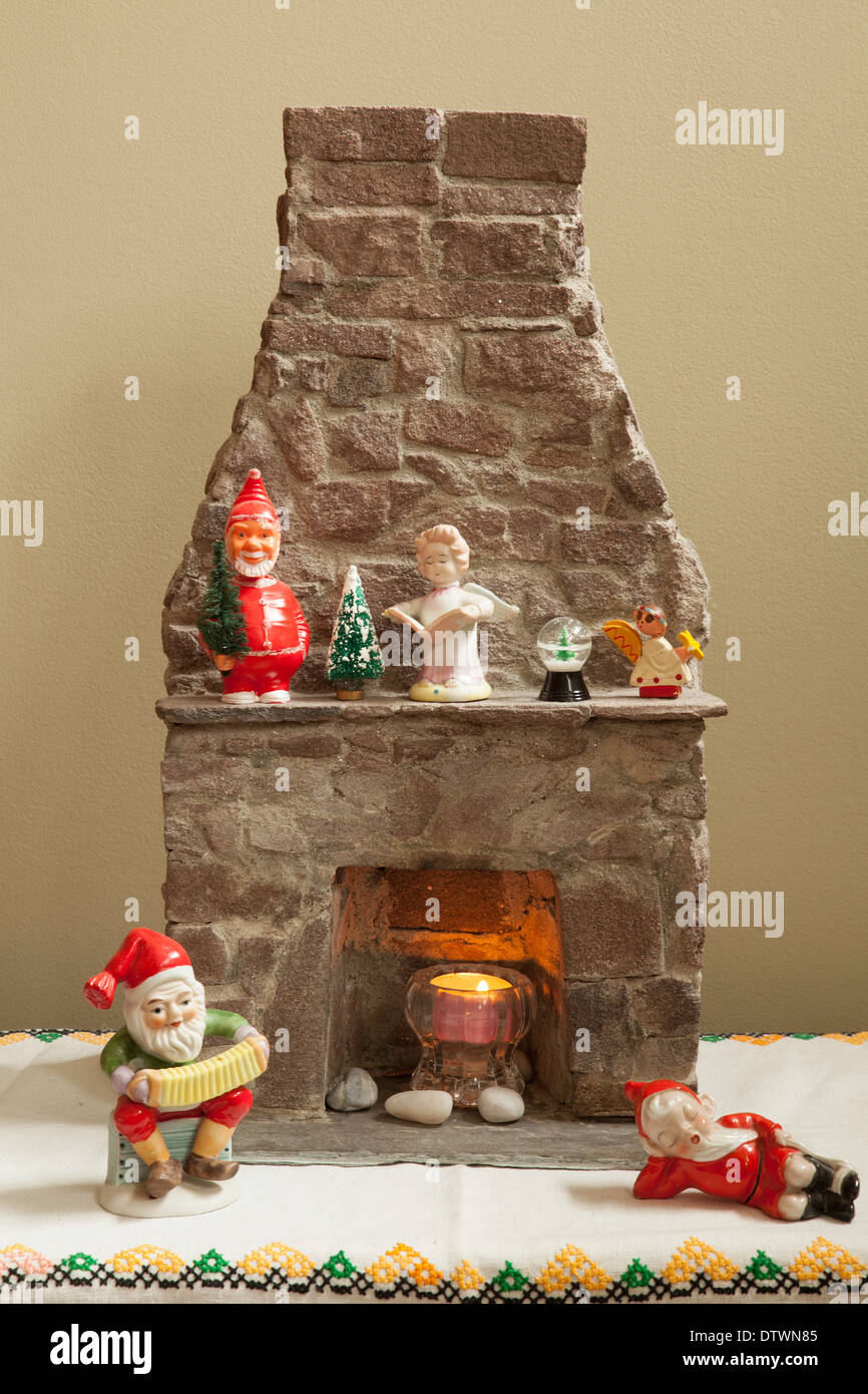 Un assortimento di decorazioni di Natale intorno a una miniatura del caminetto in pietra, compreso un vintage Santa bobble-testa sul mantello. Foto Stock