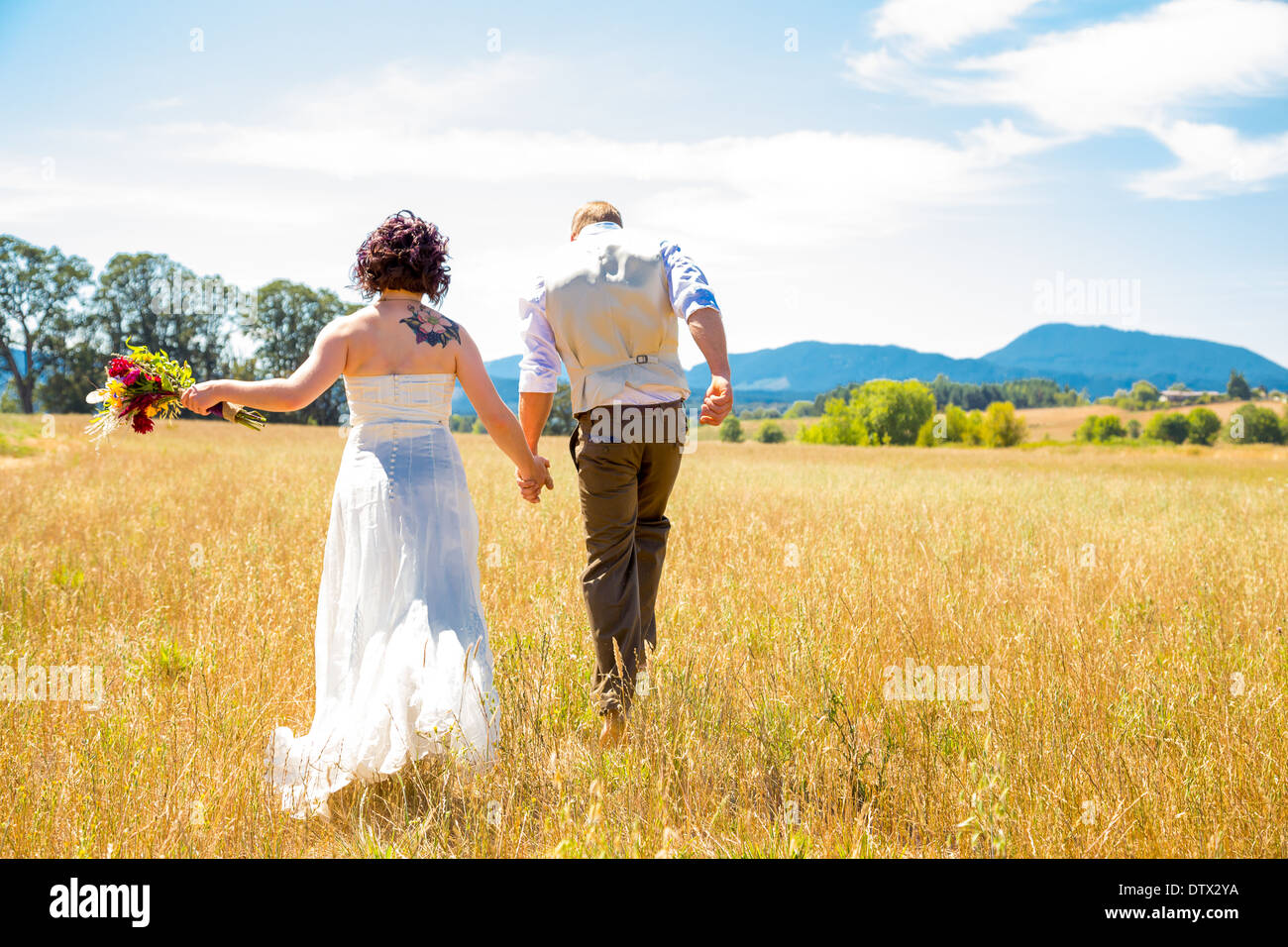 Sposa e lo sposo camminare insieme il giorno delle nozze attraverso un campo in Oregon. Foto Stock