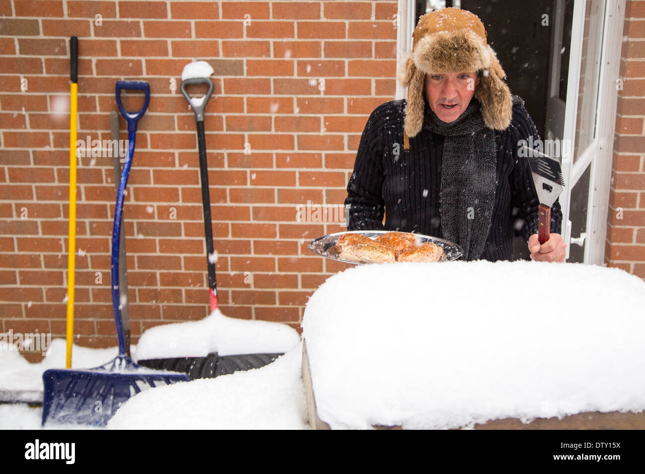 Un marito capi fuori dalla porta sul retro con un vassoio di pollo e guarda incredula al suo barbecue furono sepolti nella neve. Foto Stock