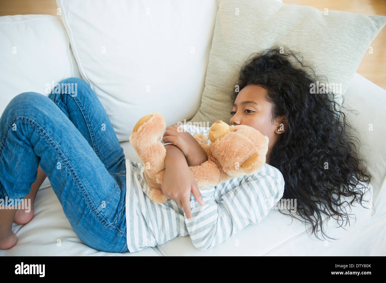 Razza mista ragazza abbracciando orsacchiotto sul divano Foto Stock