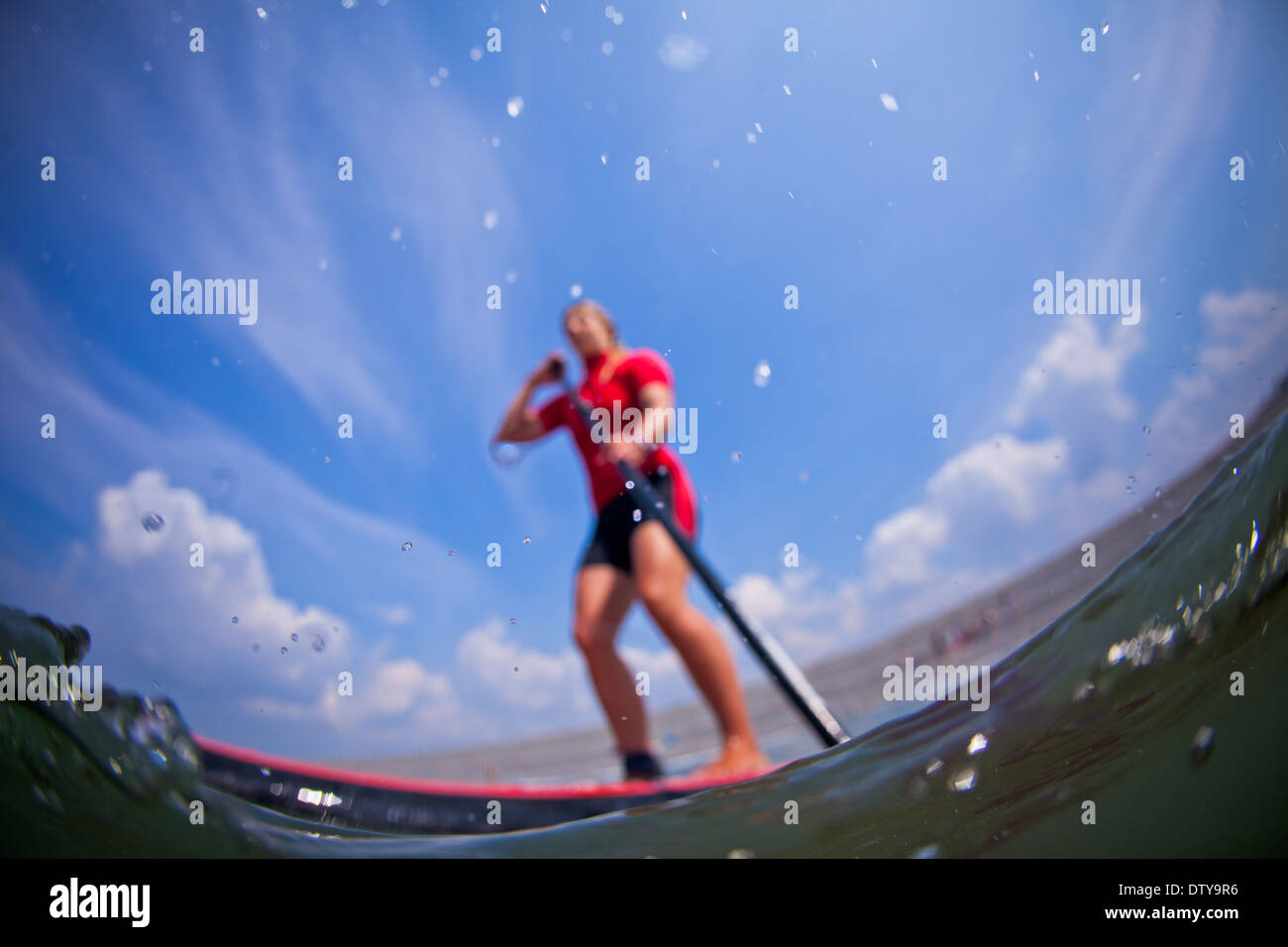 Una ragazza in una eruzione cutanea rossa vest paddleboards nelle limpide acque del North Devon UK SUP (Stand up paddleboarding) Foto Stock