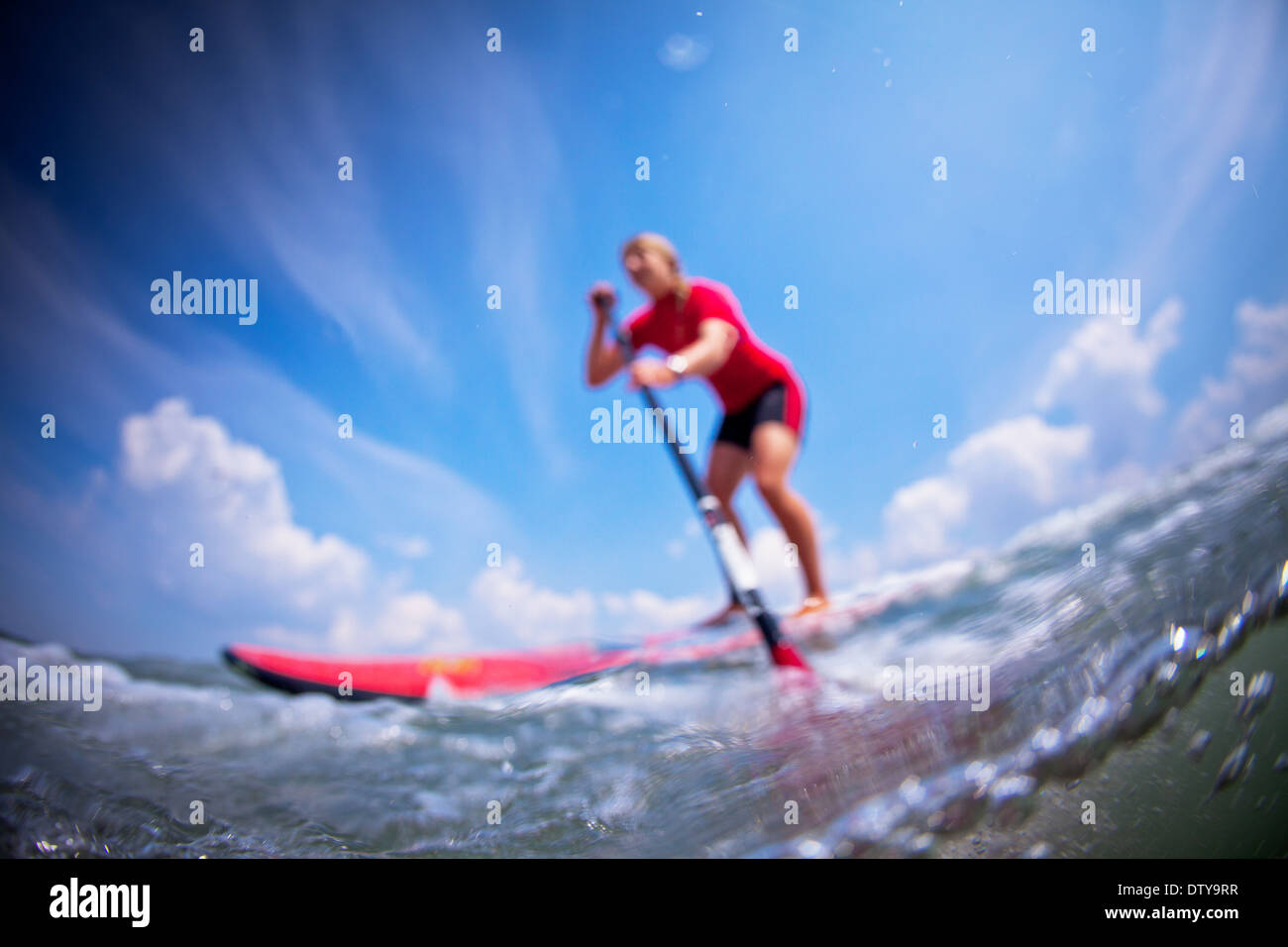 Una ragazza in una eruzione cutanea rossa vest paddleboards nelle limpide acque del North Devon UK SUP (Stand up paddleboarding) Foto Stock