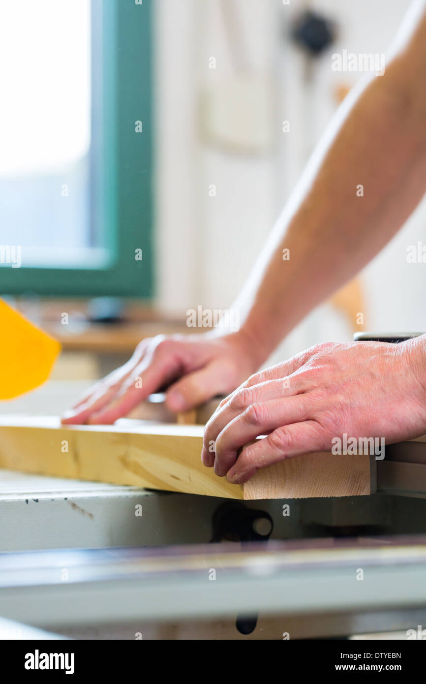 Carpenter lavorando su un ronzio elettrico visto e il taglio di alcuni pannelli in falegnameria Foto Stock