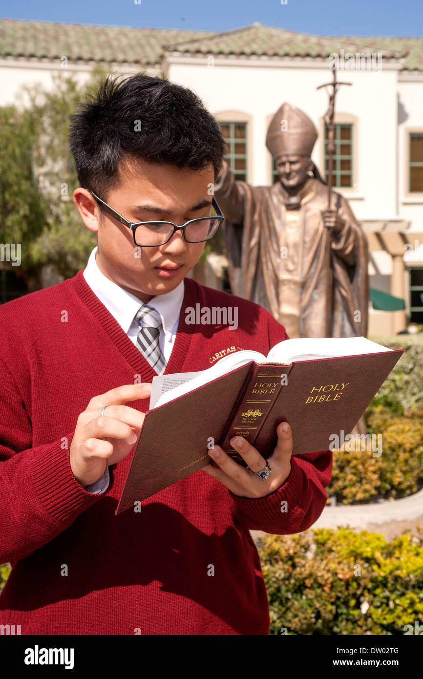 Un uniformata asiatica di studenti americani legge la Bibbia sul campus di un privato Catholic High School in San Juan Capistrano, CA. Foto Stock