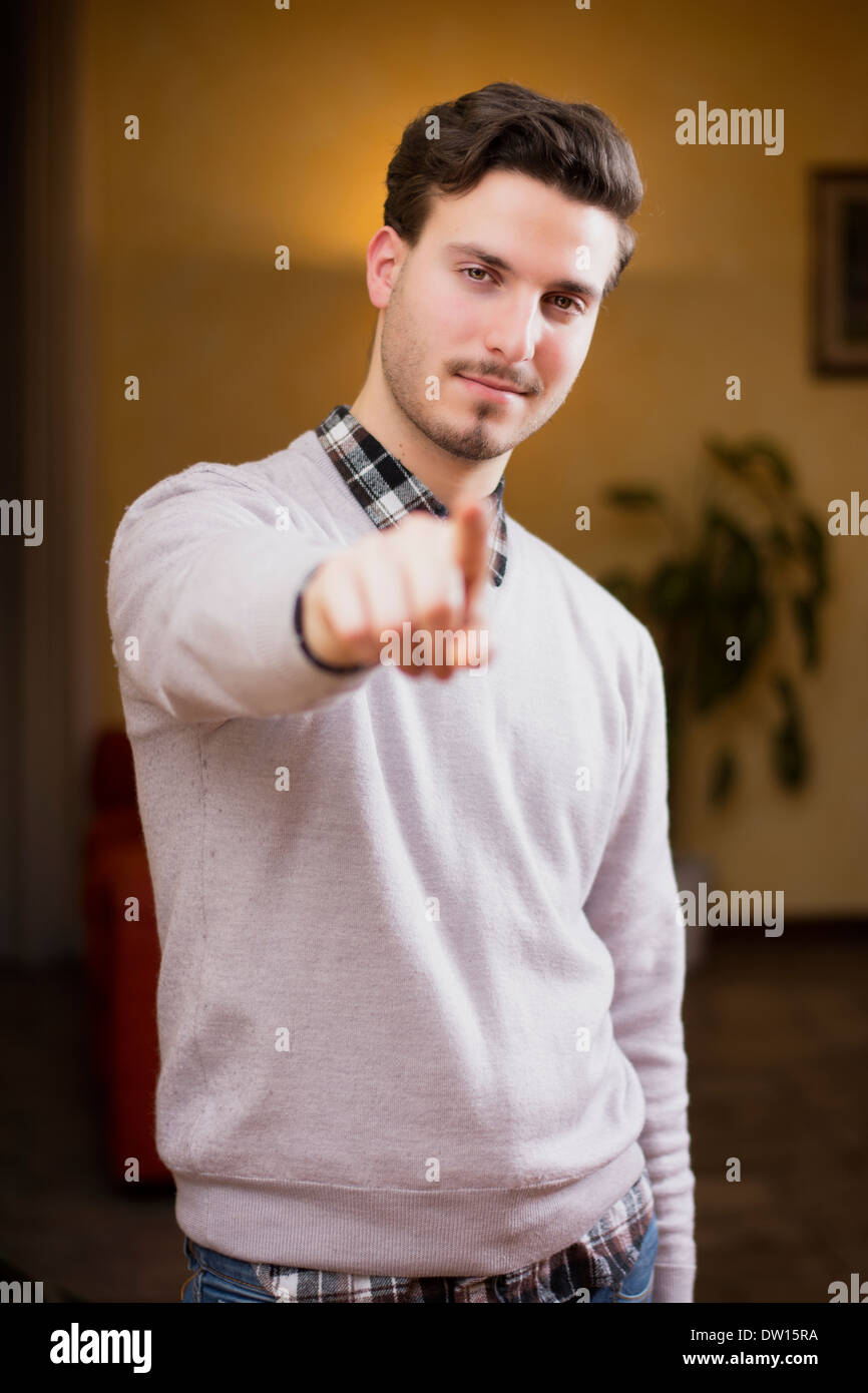 Bel giovane puntare il dito a voi, sorridente. Riprese in interni all'interno di una casa Foto Stock