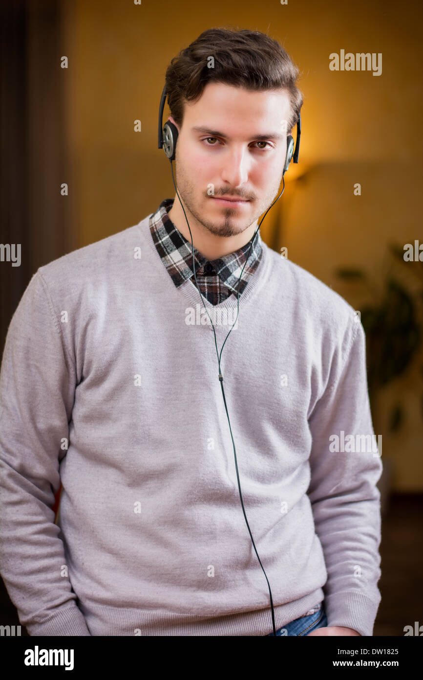 Attraente giovane uomo ascoltare musica su cuffie a casa, guardando la telecamera, gravi Foto Stock