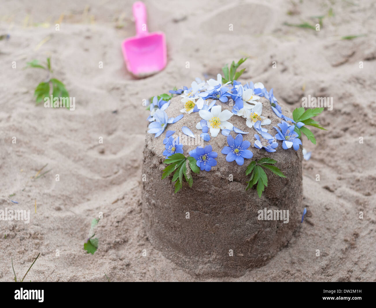 Torta di sabbia con piccole decorazioni di fiori di bambini sandbox Foto Stock