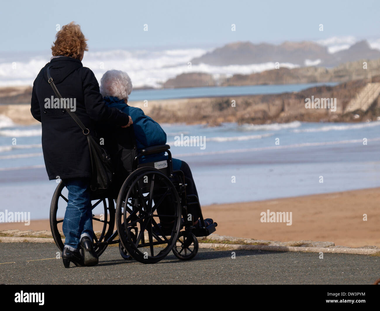La donna in sedia a rotelle helper e guardando il mare, Bude Cornwall, Regno Unito Foto Stock