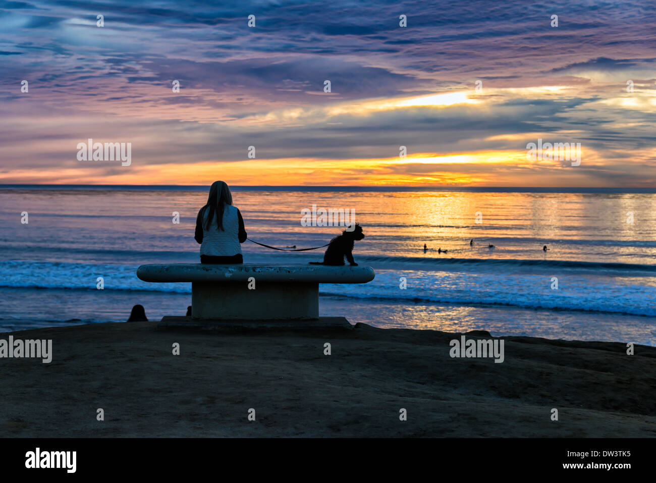 Una persona e un cane seduta su una panchina. Vibrante il tramonto visto da Sunset Cliffs parco naturale. San Diego, California, Stati Uniti. Foto Stock