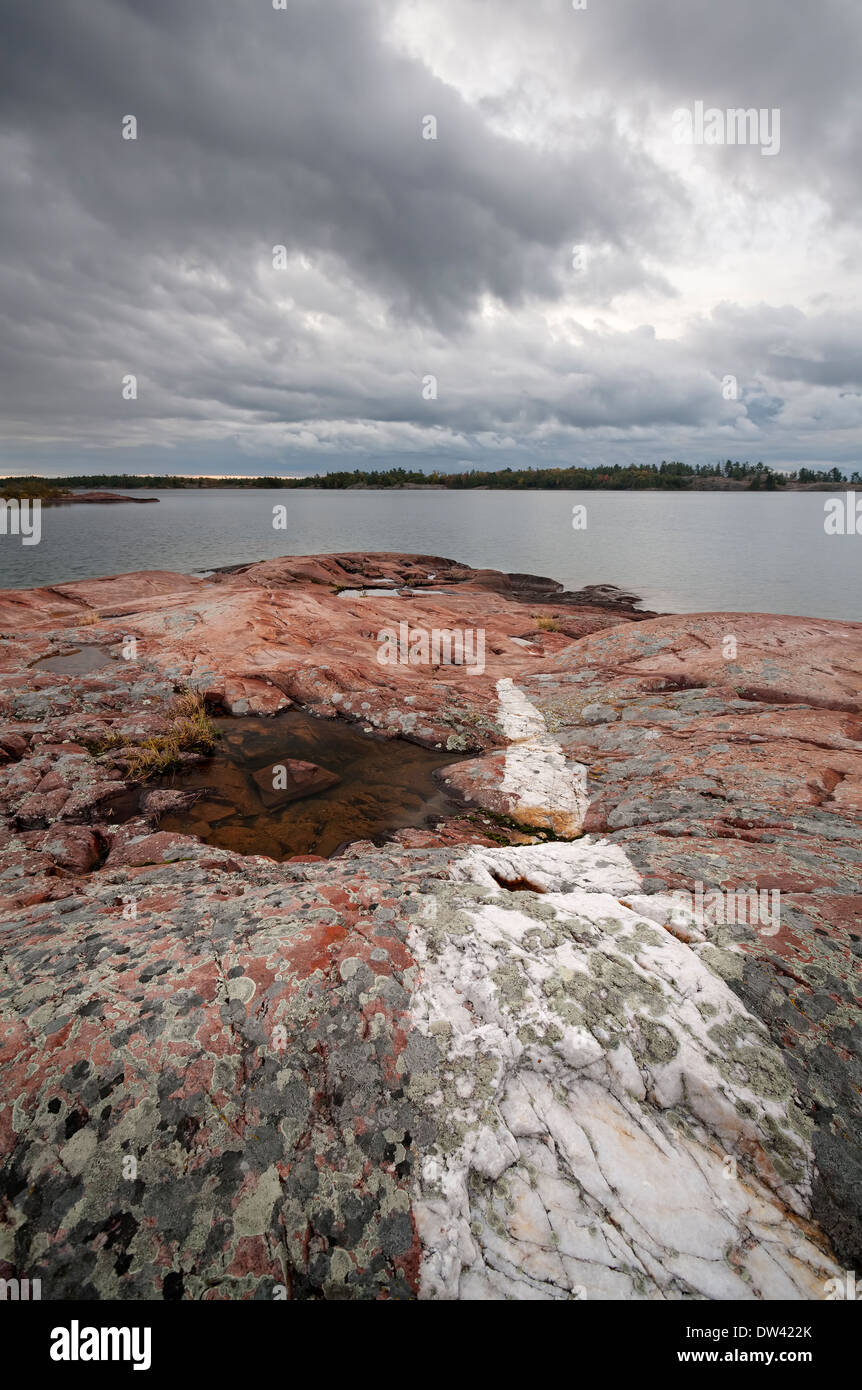 Licheni crescono su Quarzite rosa rock sotto pesante nuvola grigio in Killarney Provincial Park, Ontario, Canada. Foto Stock