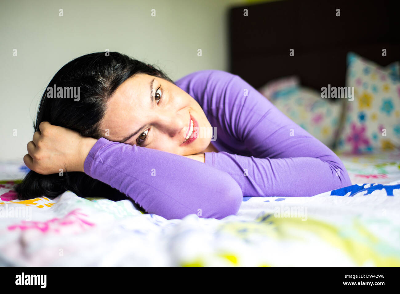 Donna sorridente che giace nel suo letto nella luce del giorno Foto Stock