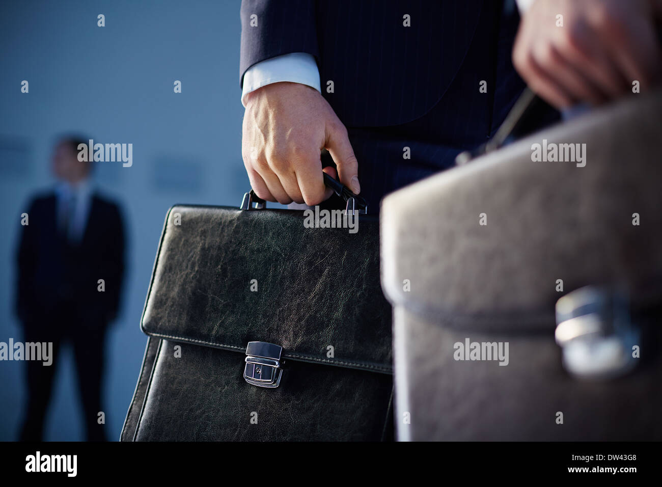 Immagine ritagliata di partner commerciali che trasportano valigette in primo piano mentre il loro collega in piedi sullo sfondo Foto Stock