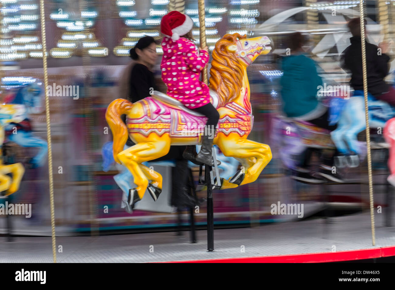 Madre guarda la figlia giri a cavallo su merry-go-round Foto Stock