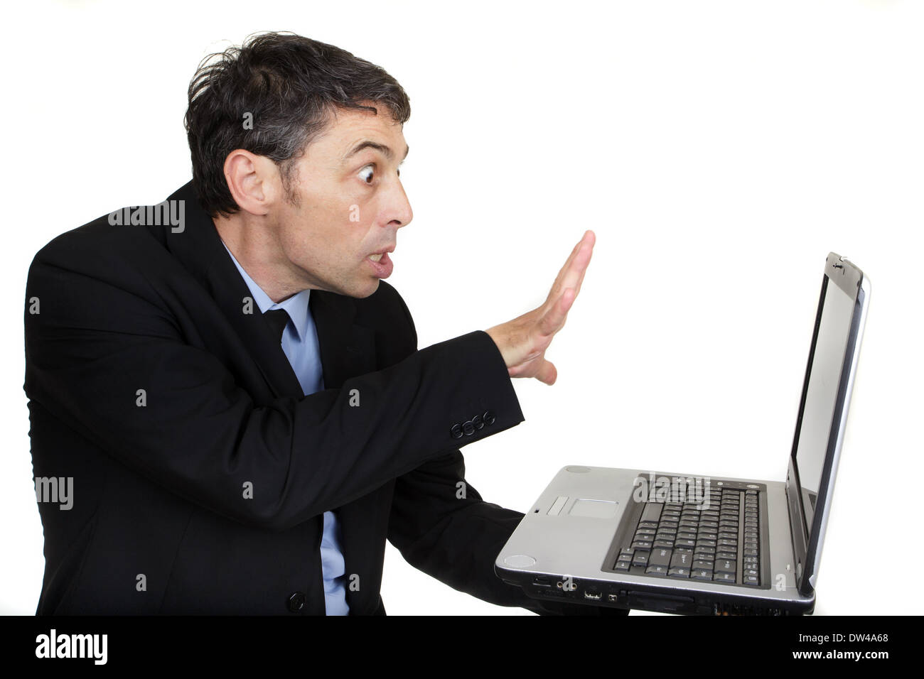 Imprenditore colata di un incantesimo sul suo computer portatile tenendolo con una mano mentre gesticolando con la sua mano distesa in corrispondenza dello schermo Foto Stock
