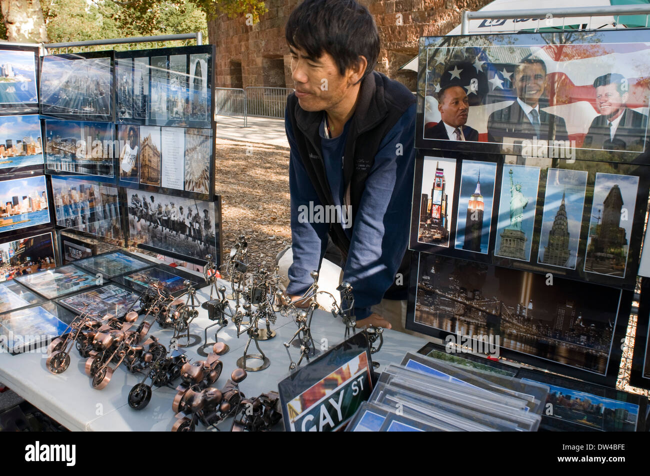 Un uomo che sta dietro una grande mostra di foto, segni e altri souvenir di New York a Battery Park. Venditore a vendere cartoline Foto Stock