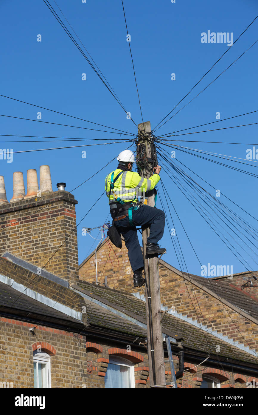 Ingegnere delle Telecomunicazioni lavorando su un overhead di comunicazioni telefoniche pole tra case a schiera a Londra, Regno Unito Foto Stock