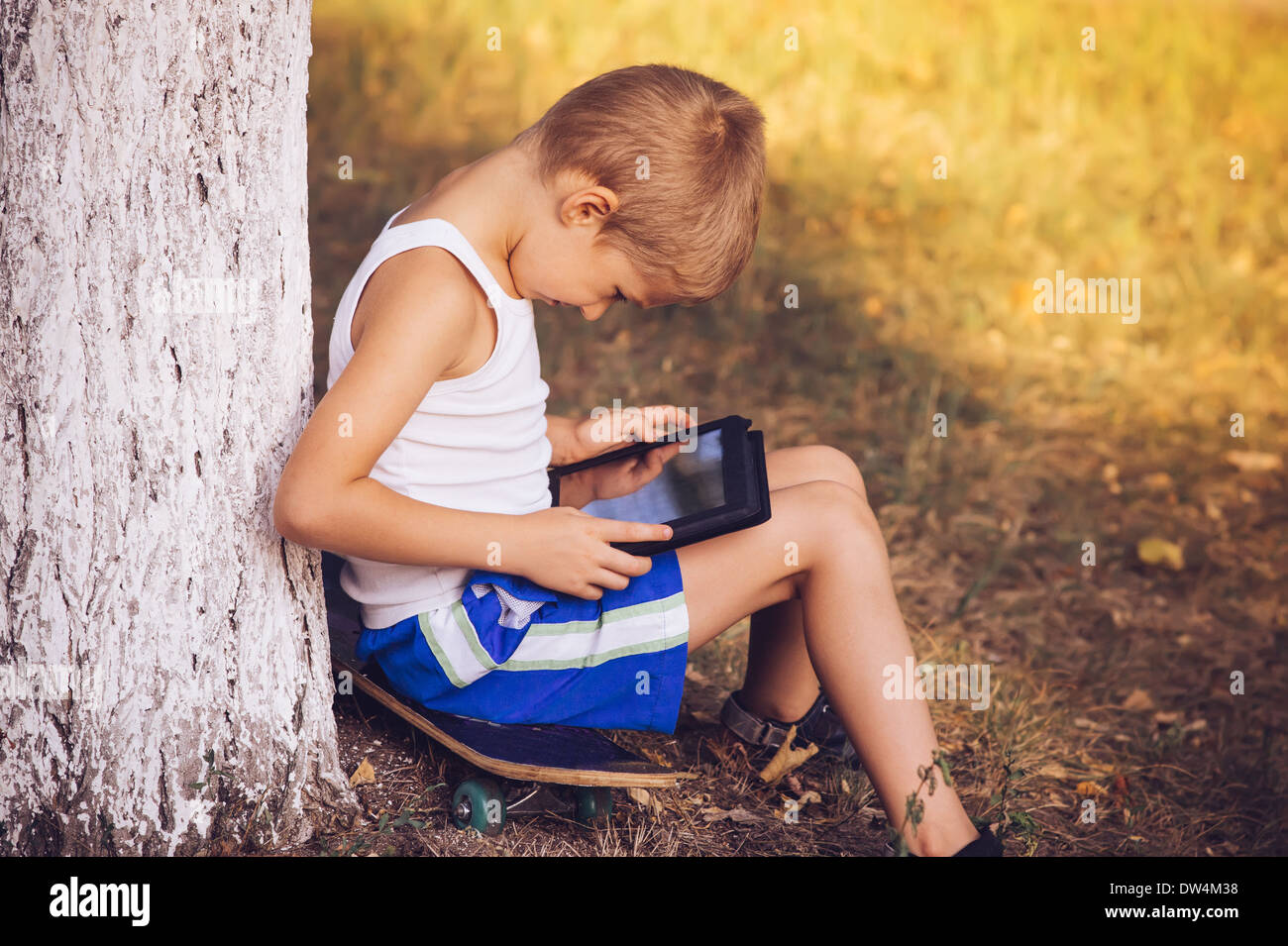 Ragazzo bambino che gioca con i Tablet PC esterno con estate natura su sfondo Computer Game dipendenza concetto Lifestyle Foto Stock