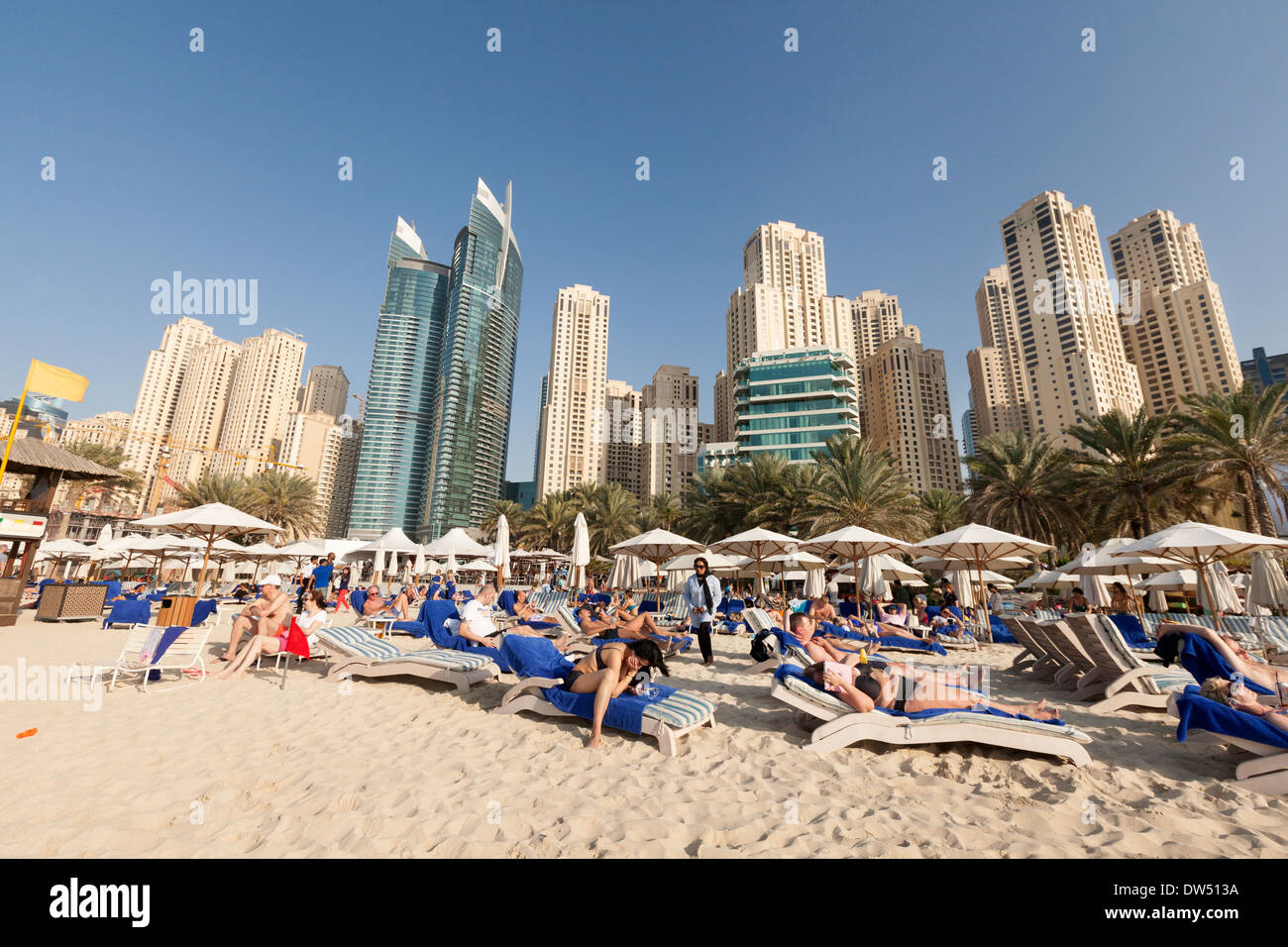Vacanza Dubai; la folla di turisti in vacanza a prendere il sole sulla spiaggia di Jumeirah in inverno, Hilton Hotel , Dubai, Emirati Arabi Uniti, Emirati Arabi Uniti, Medio Oriente Foto Stock