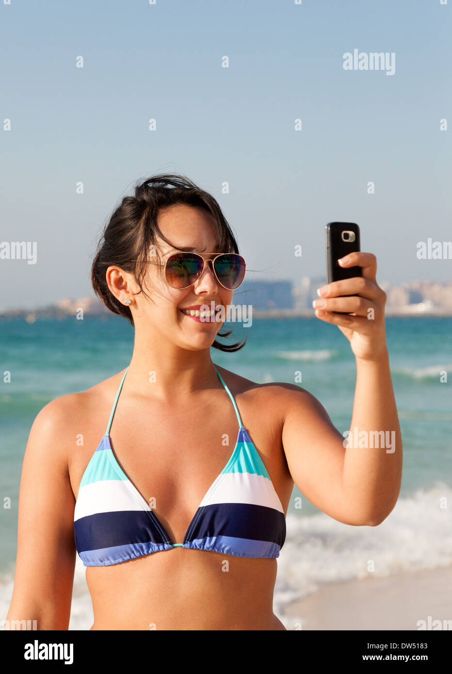 Donna prendendo una foto selfie sulla spiaggia in un bikini in vacanza sulla spiaggia di Jumeirah, Dubai, Emirati Arabi Uniti, Emirati arabi uniti, Medio Oriente Foto Stock