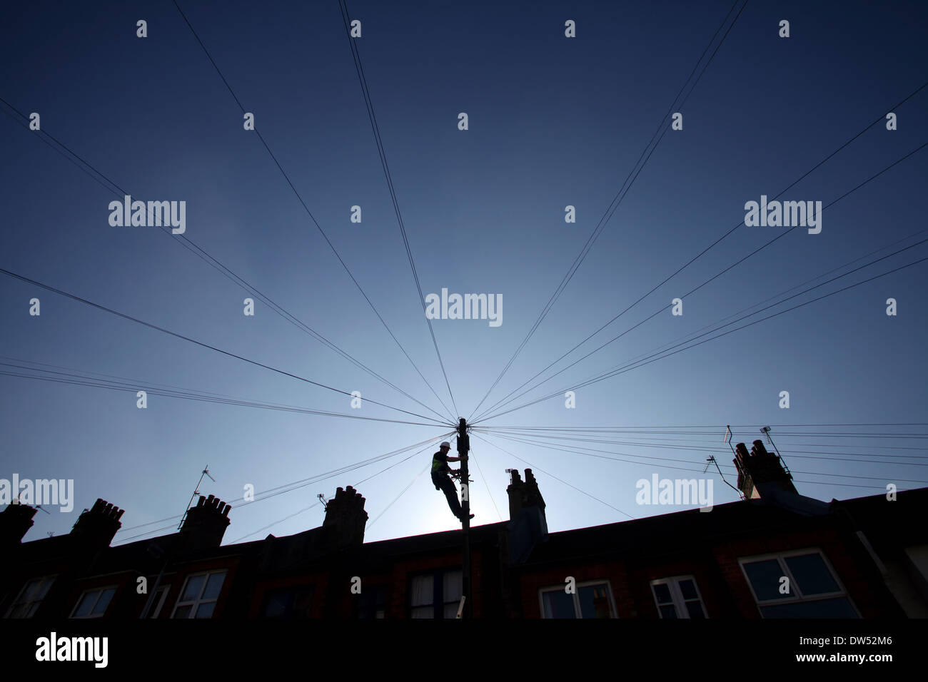 Un ingegnere delle telecomunicazioni fissa i fili nella parte superiore di un sondaggio telefonico / stagliano dal sole Foto Stock