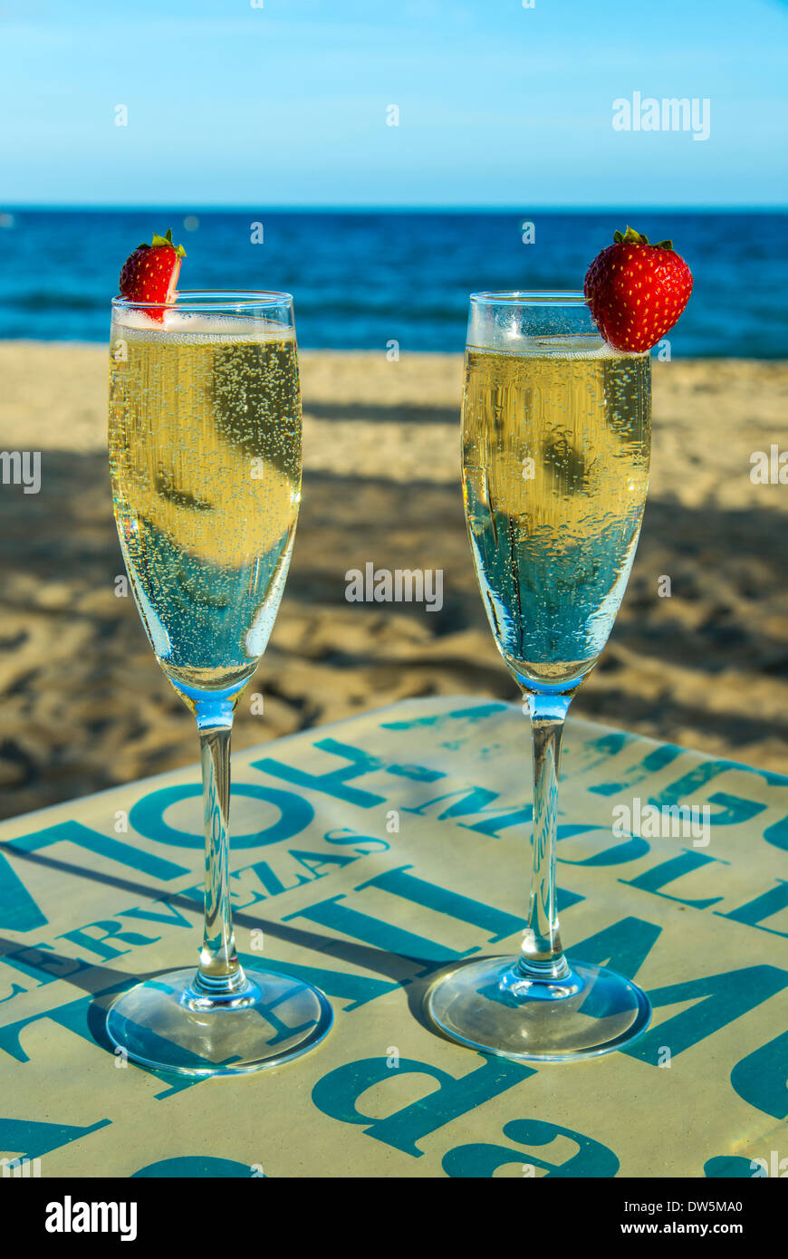 Due bicchieri di vino spumante sul tavolo con spiaggia di sabbia e il mare in background Foto Stock