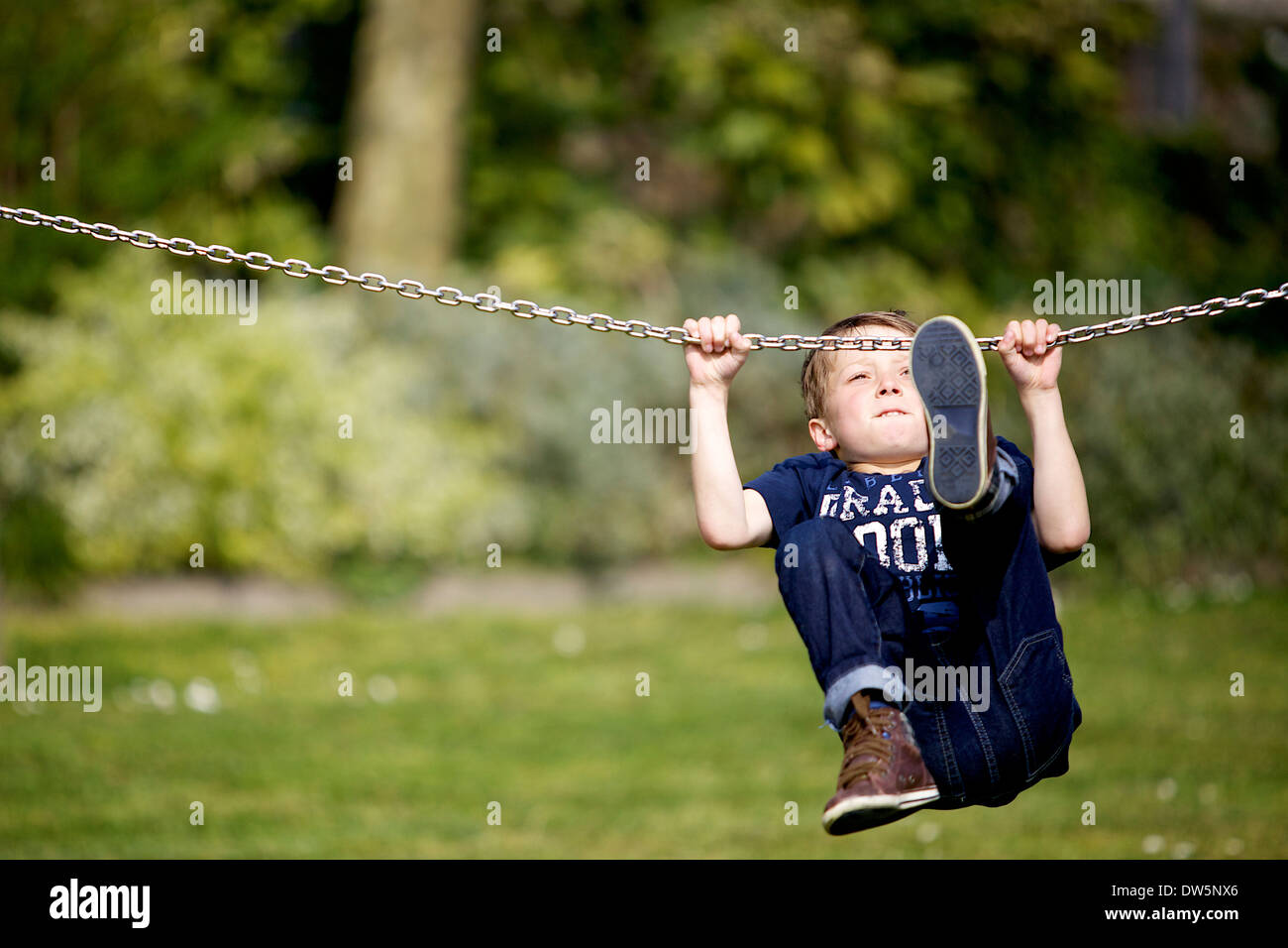 Bambino di circa 10 anni determinato a non lasciare andare catena sul parco giochi per bambini. Foto Stock