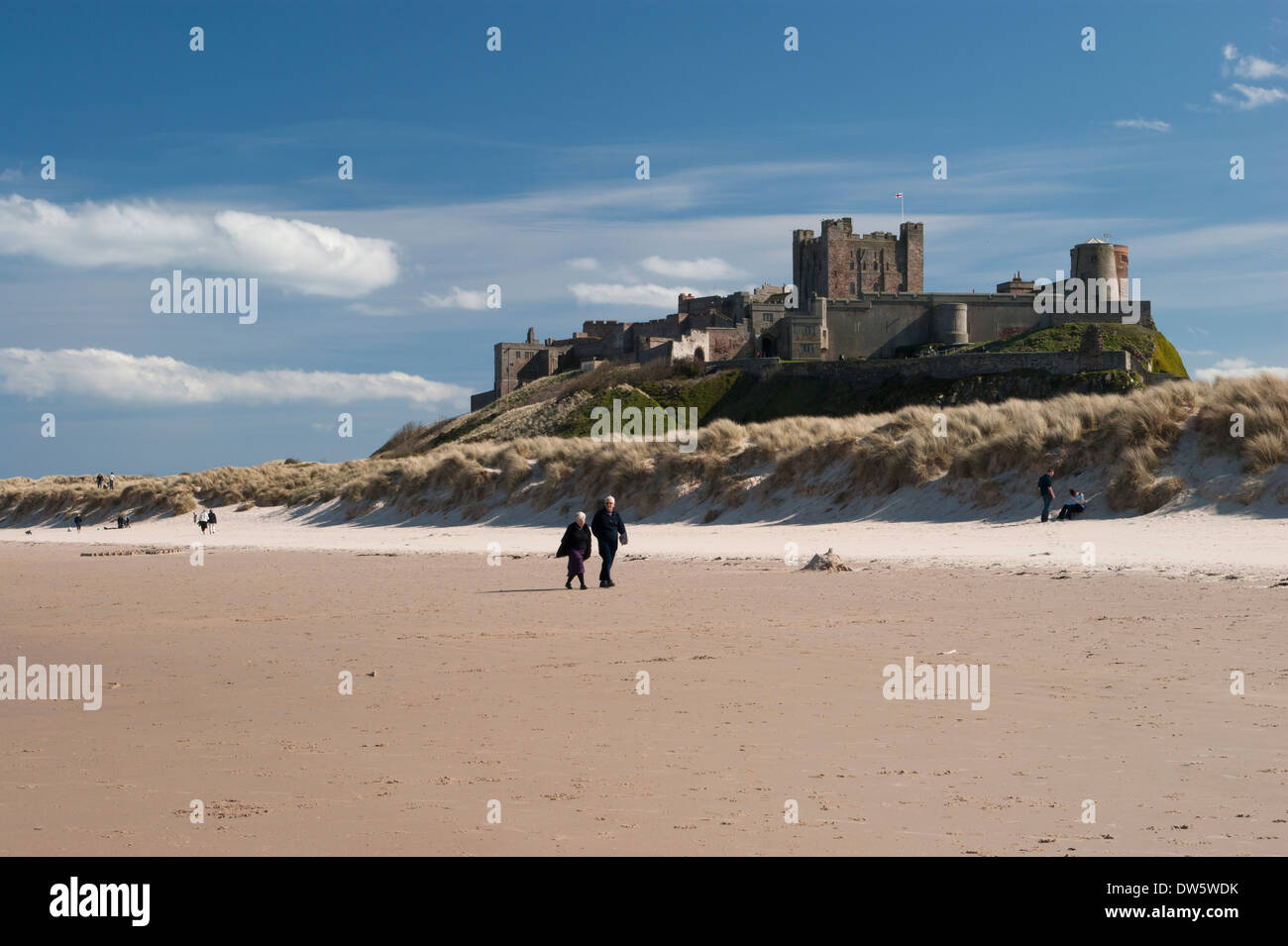 Il castello di Bamburgh sulla costa Northumbrian, Inghilterra, shot dalla spiaggia sotto un luminoso cielo blu. Foto Stock