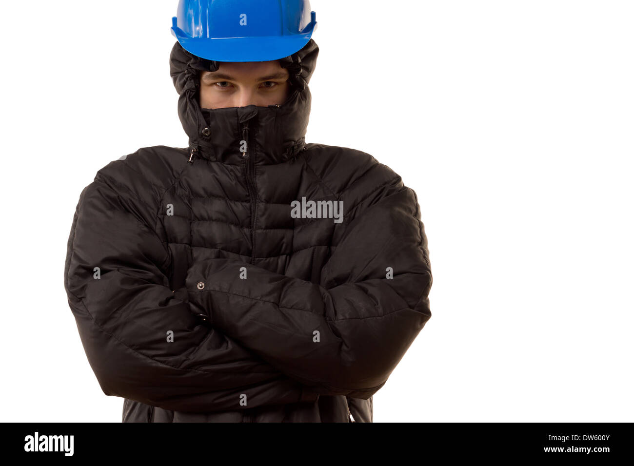 Combattivo giovane thug in un nero passamontagna e permanente hardhat bloccando la strada con una espressione arrabbiato e con bracci ripiegati, Foto Stock