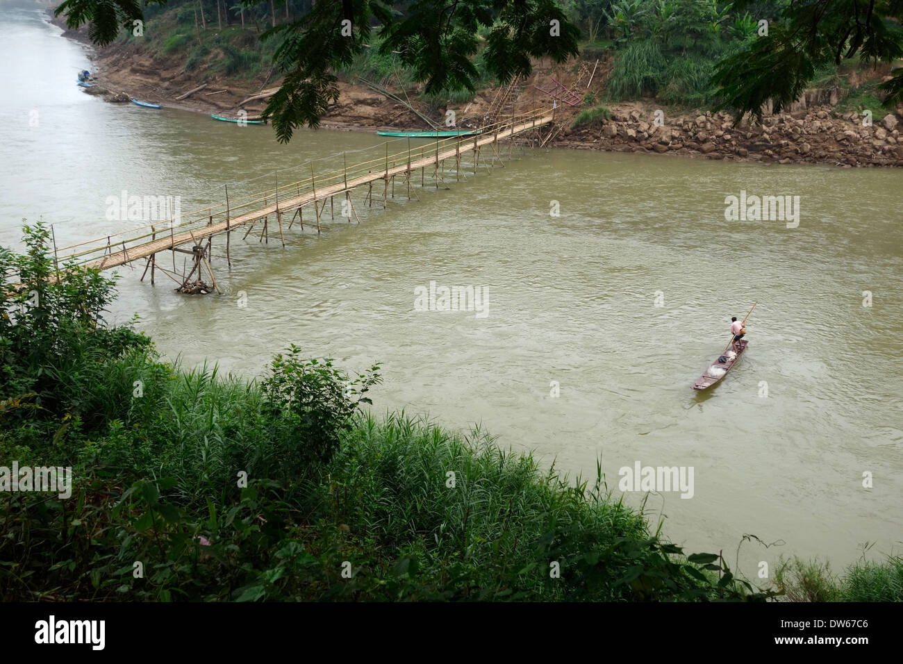 Il laotiano pescatore la polarizzazione la sua barca al di sopra del bambù stagionale ponte sul Nam Fiume Kahn a Luang Prabang, Laos. Foto Stock