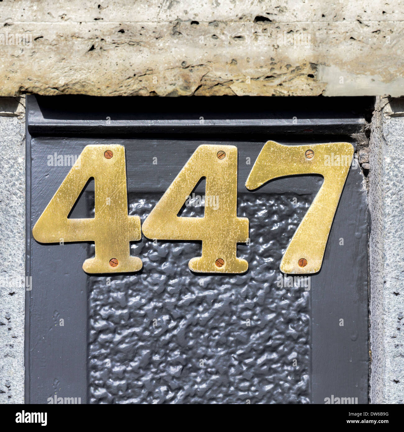Casa di ottone numero quattro cento quaranta sette, avvitate contro un muro grigio Foto Stock