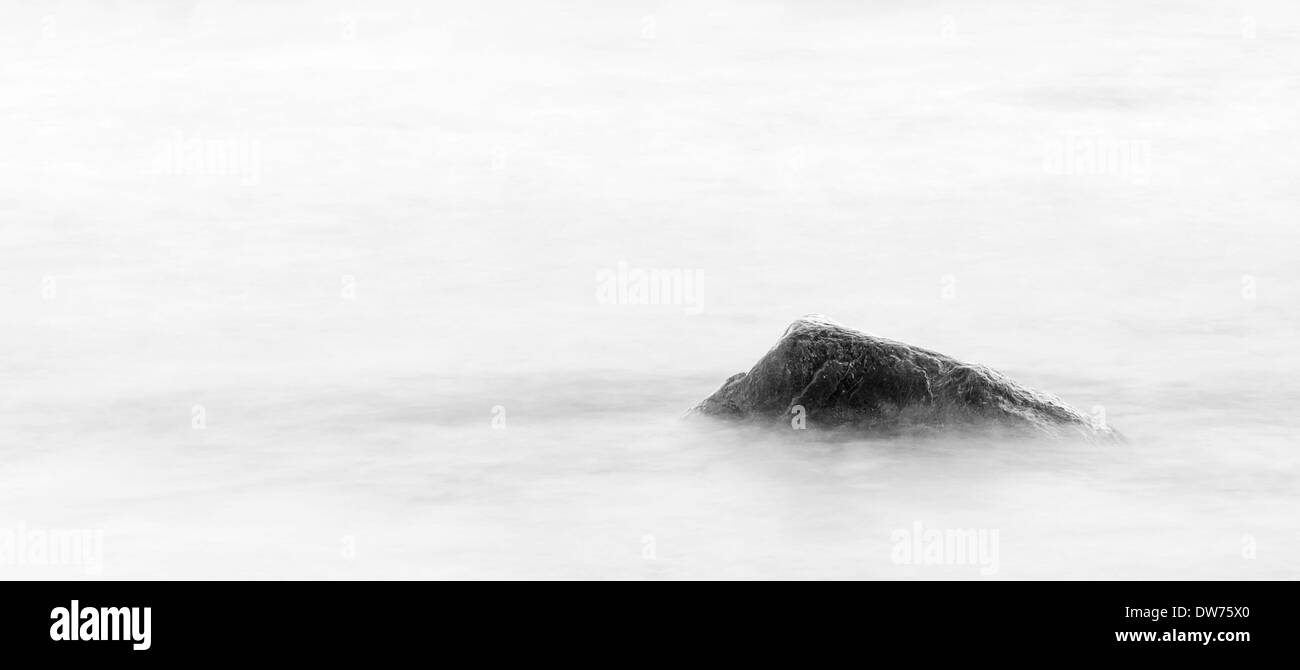 Singola pietra o roccia in un mare sfocato Foto Stock