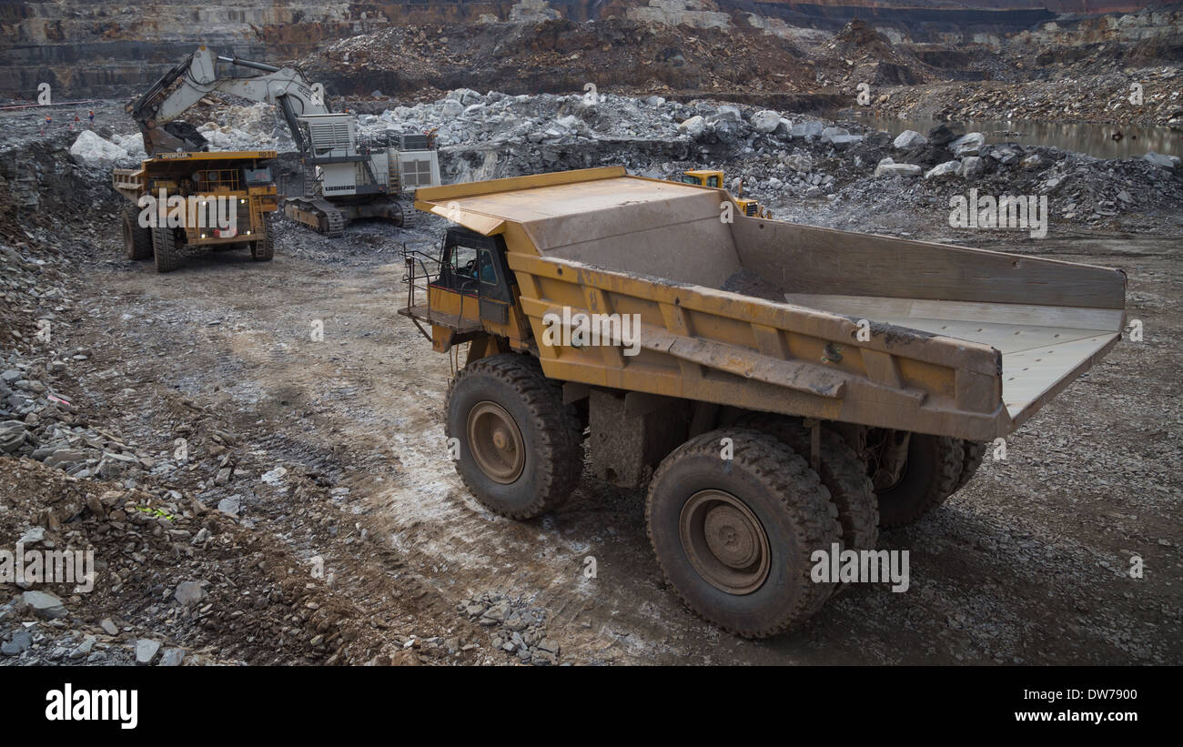 Caterpillar carrello minerario attende in linea mentre un escavatore liebherr minerale di carichi in un camion in background Foto Stock