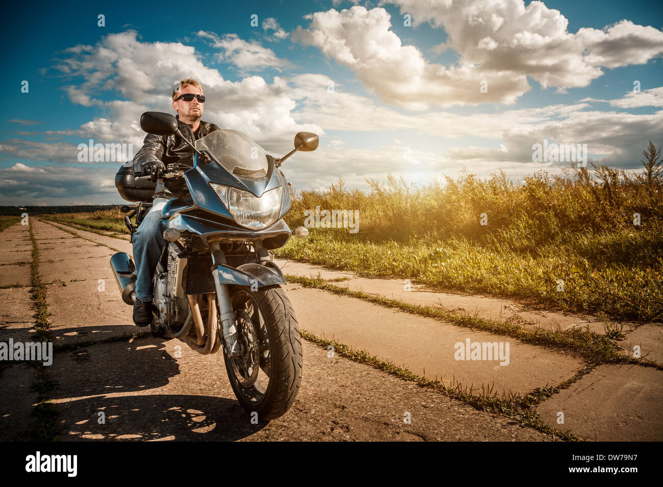 Biker uomo che indossa una giacca di pelle e occhiali da sole seduto sulla sua moto guardando il tramonto. Foto Stock
