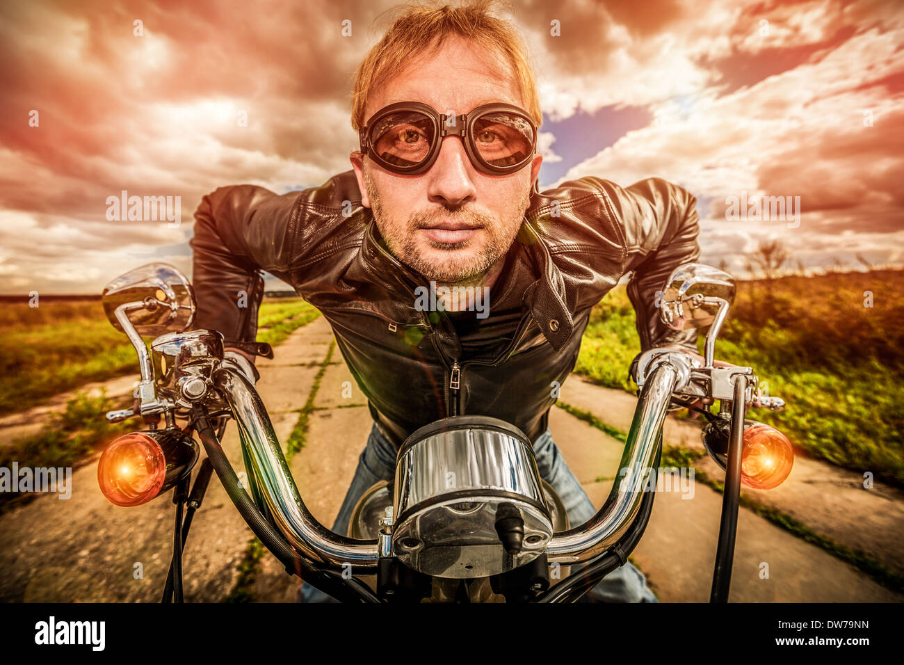Funny Biker in occhiali da sole e giacca di pelle racing su strada (obiettivo fisheye). Filtro applicato in post-produzione. Foto Stock Funny Biker in occhiali da sole e giacca di pelle racing su strada (obiettivo fisheye). Filtro applicato in post-produzione. Foto Stock