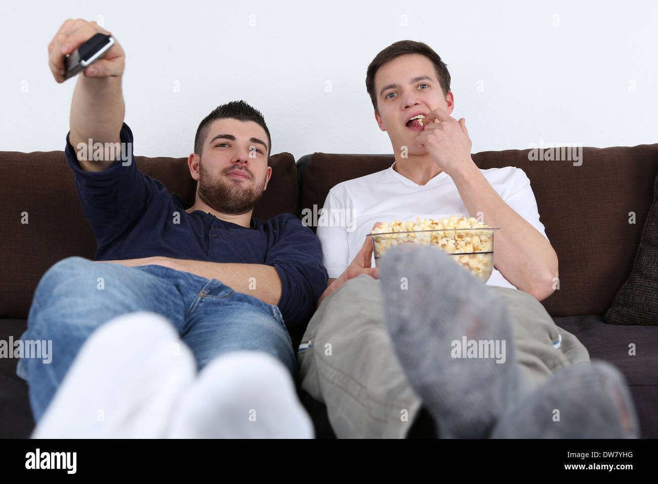 Giovani seduto su un divano, rilassante e mangiare popcorn mentre guardi la TV Foto Stock