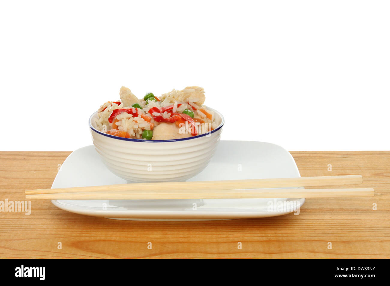 Pasto cinese di pollo e riso vegetale in una ciotola con bacchette su una tavola di legno contro uno sfondo bianco Foto Stock