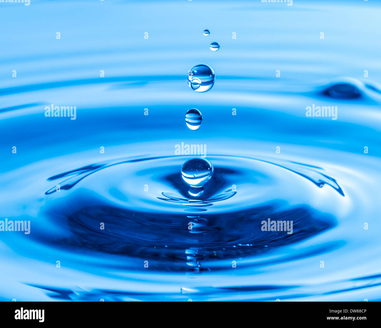Una gocciolina d'acqua dopo aver colpito e rimbalzano fuori acqua, su uno sfondo blu. Foto Stock