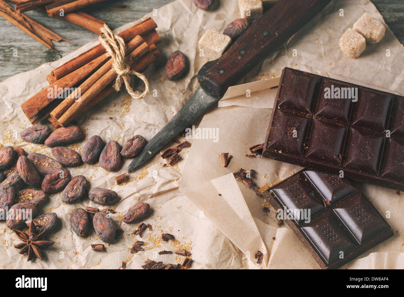 Vista dall'alto sul cioccolato fondente con il vecchio coltello, le fave di cacao, cannella e anice su carta sgualcita. Foto Stock