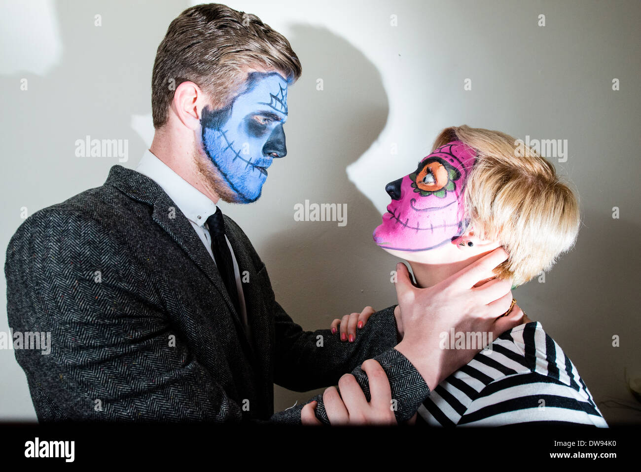 Un ben vestiti coppia giovane che indossa lo stile zombie face vernice, con l'uomo apparentemente soffoca la startled donna. Foto Stock