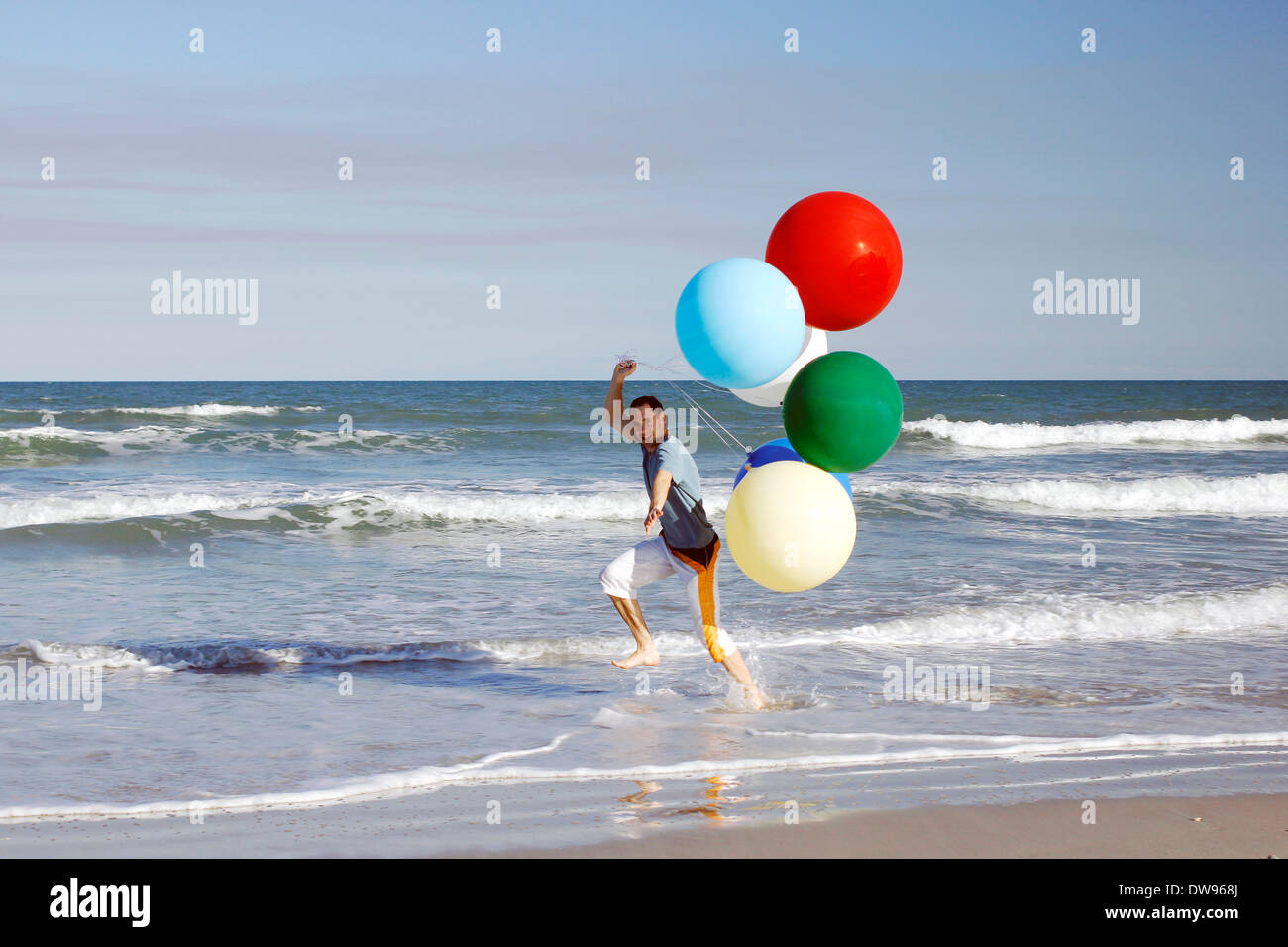 Giovane uomo con grandi palloncini colorati in spiaggia Foto Stock