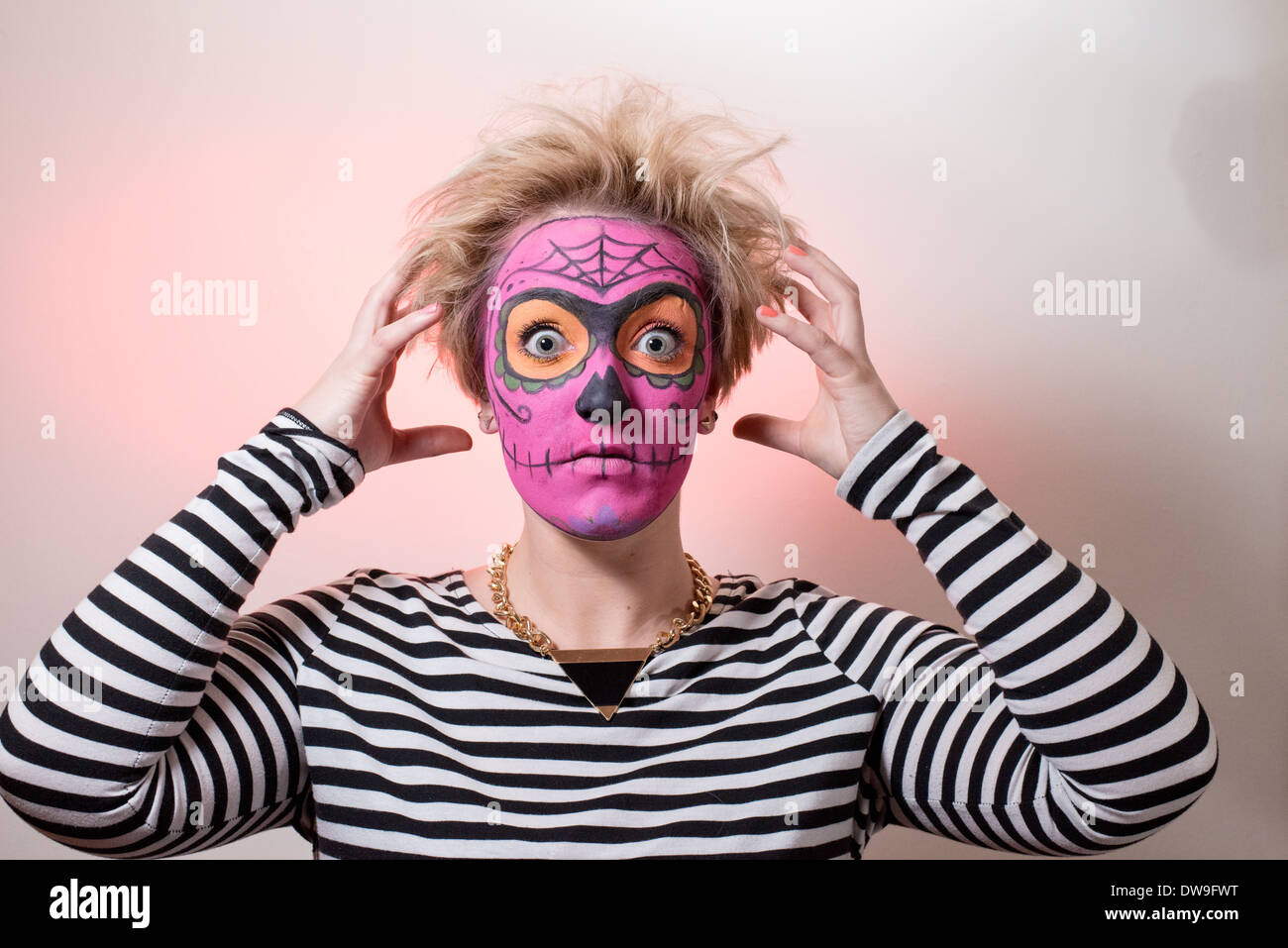 Una giovane donna con stile zombie faccia in vernice rosa e capelli selvaggi colpisce un orrore pongono per la fotocamera. Foto Stock