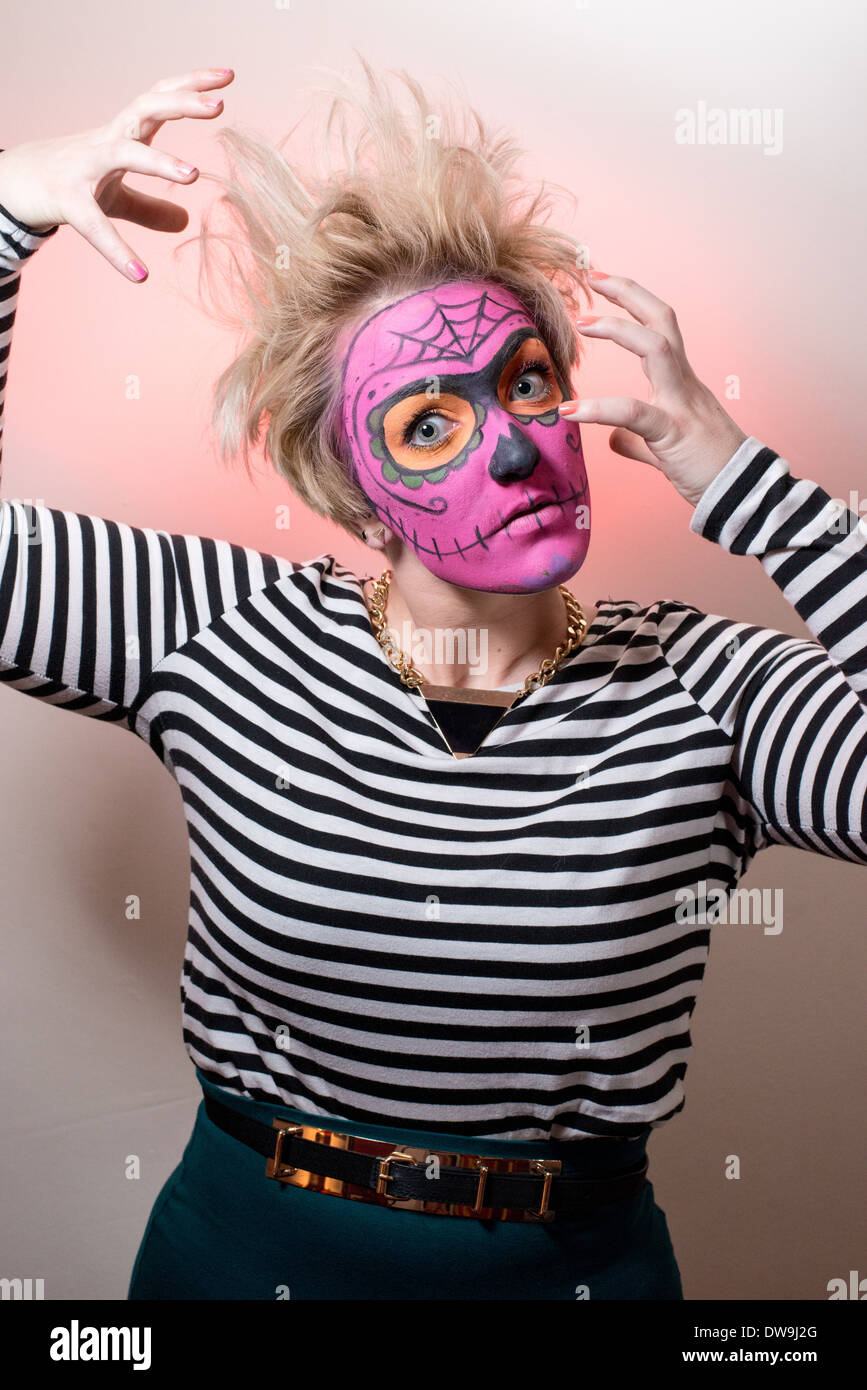 Una giovane donna con stile zombie faccia in vernice rosa e capelli selvaggi colpisce un orrore pongono per la fotocamera. Foto Stock