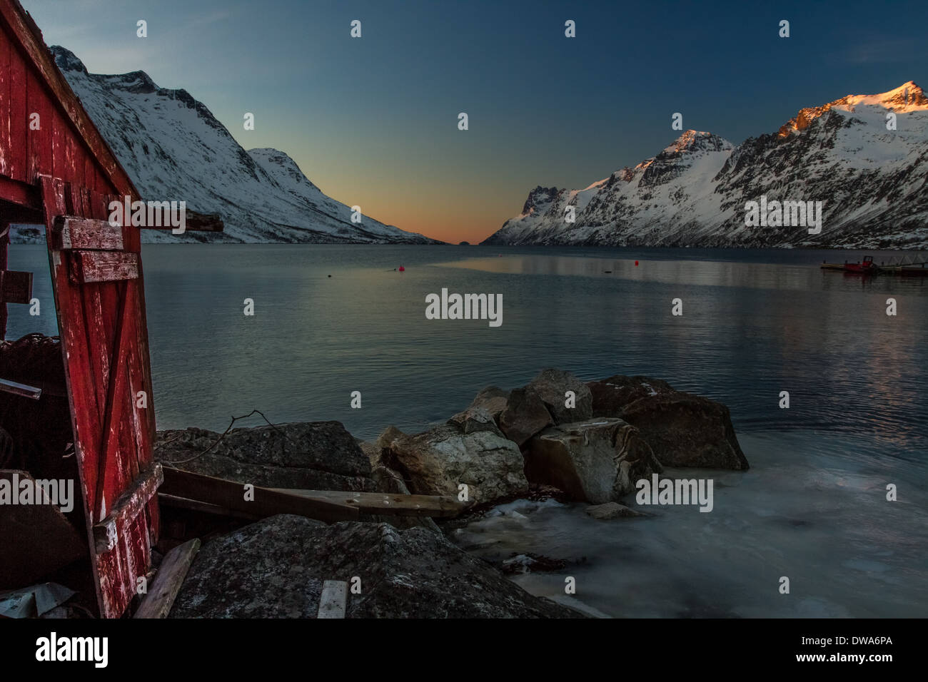 Norvegia paesaggi: lunghi tramonti sul fiordo norvegese - Ersfjordbotn con montagne innevate e capanna rosso Foto Stock