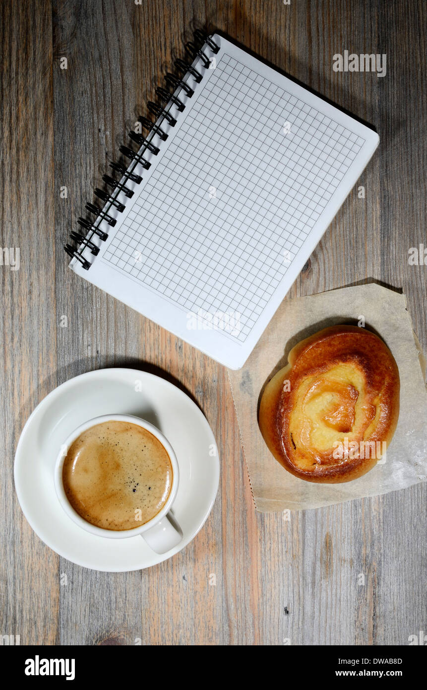 Tazza di caffè espresso, notebook a scacchi e bun su sfondo di legno Foto Stock