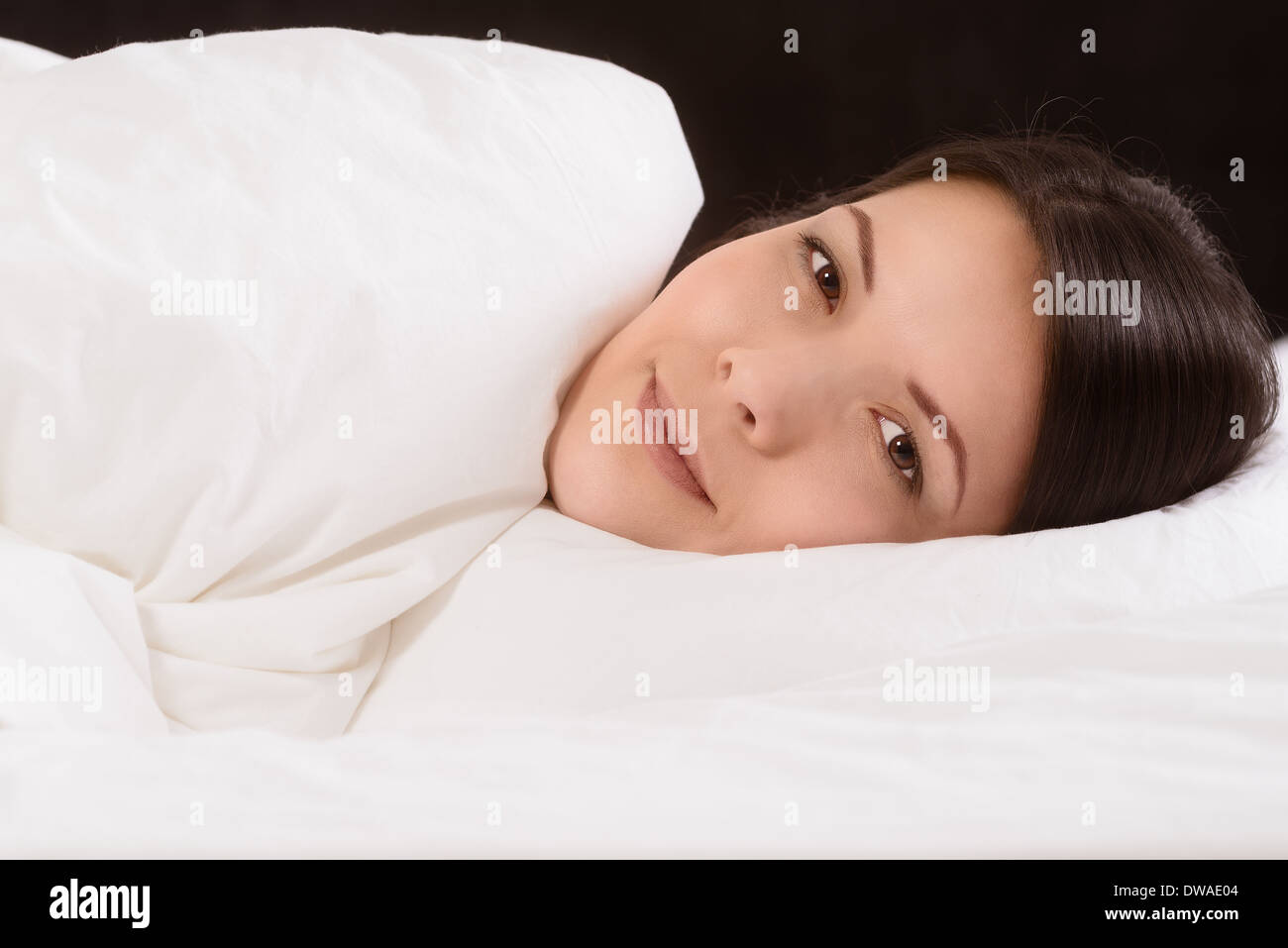 Attraente giovane donna godendo un tranquillo sonno nascosto fino a letto a sognare con un espressione serena Foto Stock