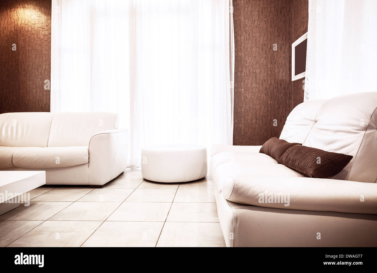 Appartamento di lusso interno in bianco&colori marrone, due elegante divano in pelle e pouf, luminoso della luce del sole attraverso la grande finestra Foto Stock