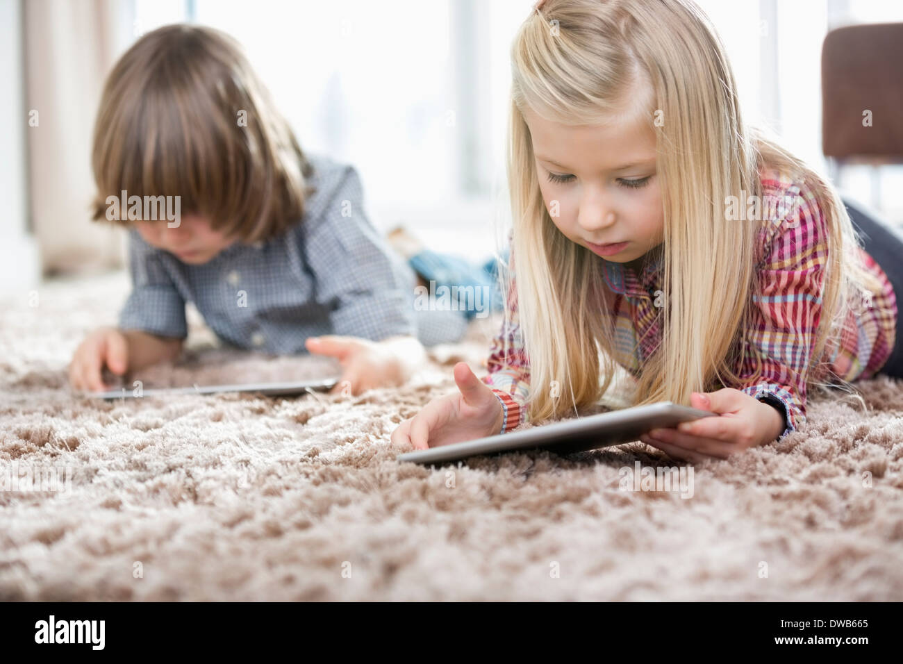 Ragazza carina e fratello utilizzando compresse digitale sul tappeto nel soggiorno Foto Stock