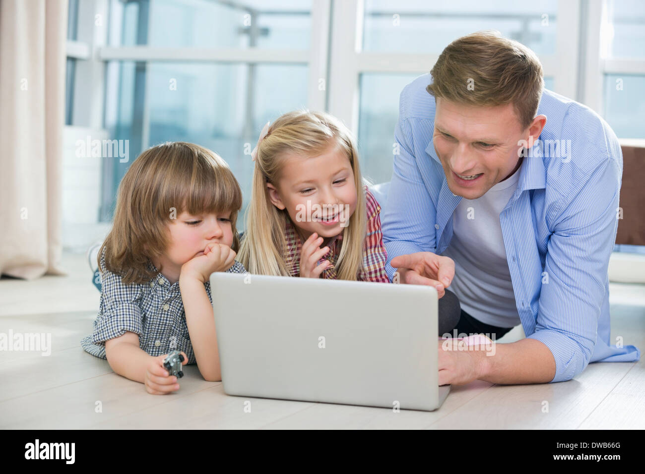 Padre Felice mostrando qualcosa per i bambini sul portatile a casa Foto Stock