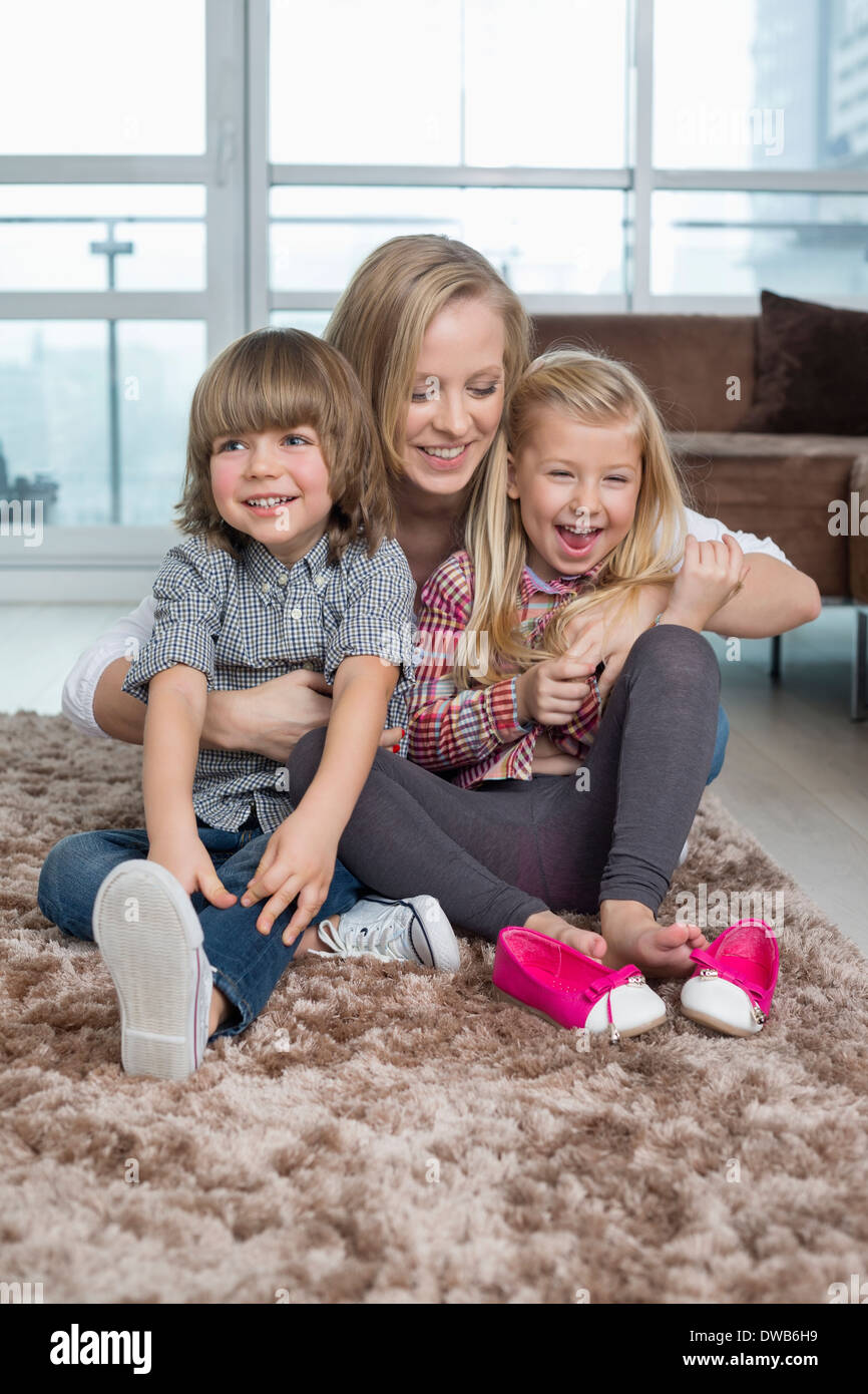 Giocoso madre con bambini seduti sul tappeto nel soggiorno Foto Stock