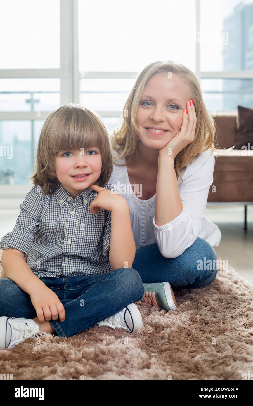 Ritratto di felice madre seduta con ragazzo sul tappeto nel soggiorno Foto Stock